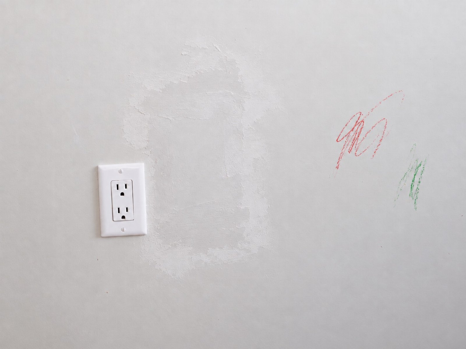 Repaired drywall patch beside an outlet, with crayon still on the wall