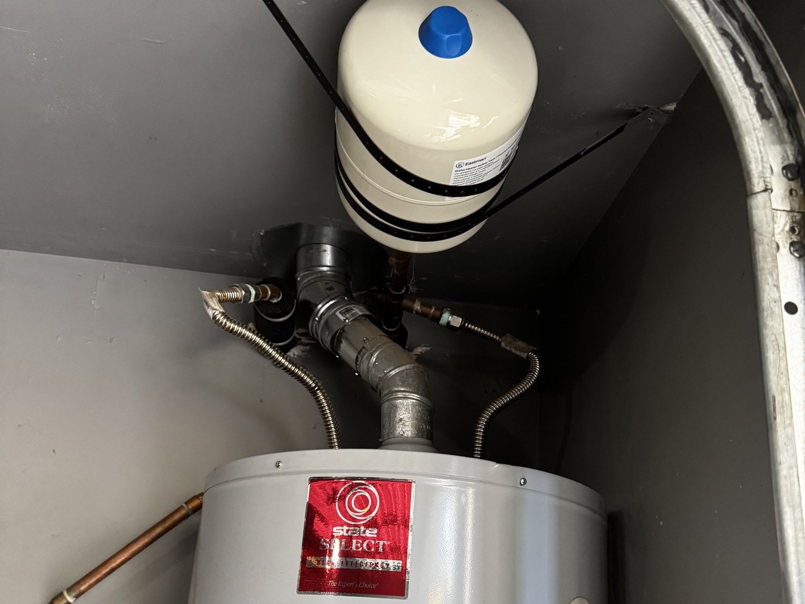 White thermal expansion tank with a blue cap mounted above a water heater